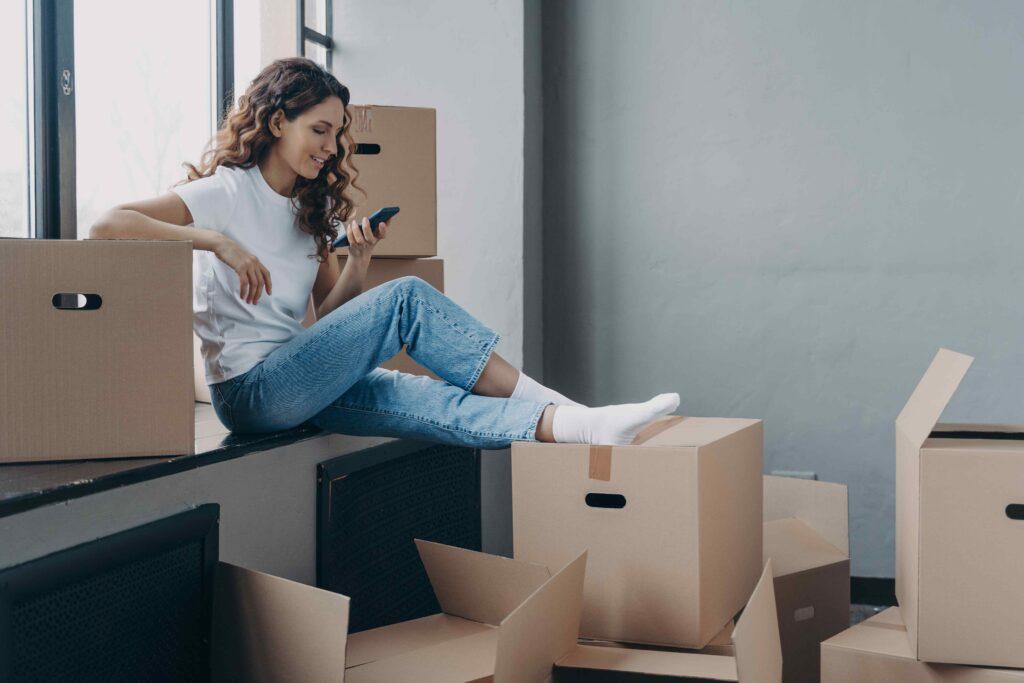 Woman checking her phone while surrounded by moving boxes